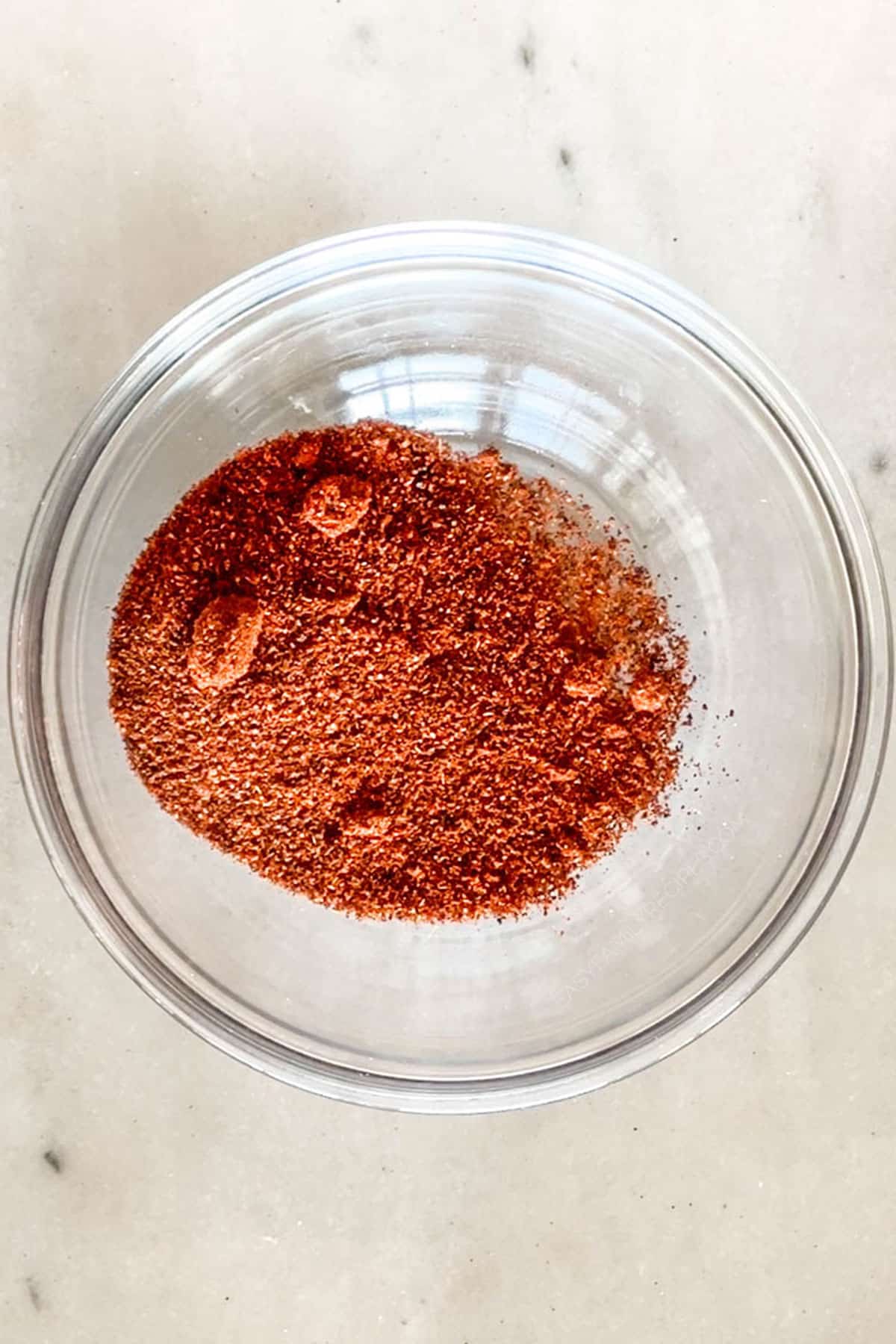 Step one for making Carne Asada Seasoning Blend- chili powder in a clear bowl. On a wooden background