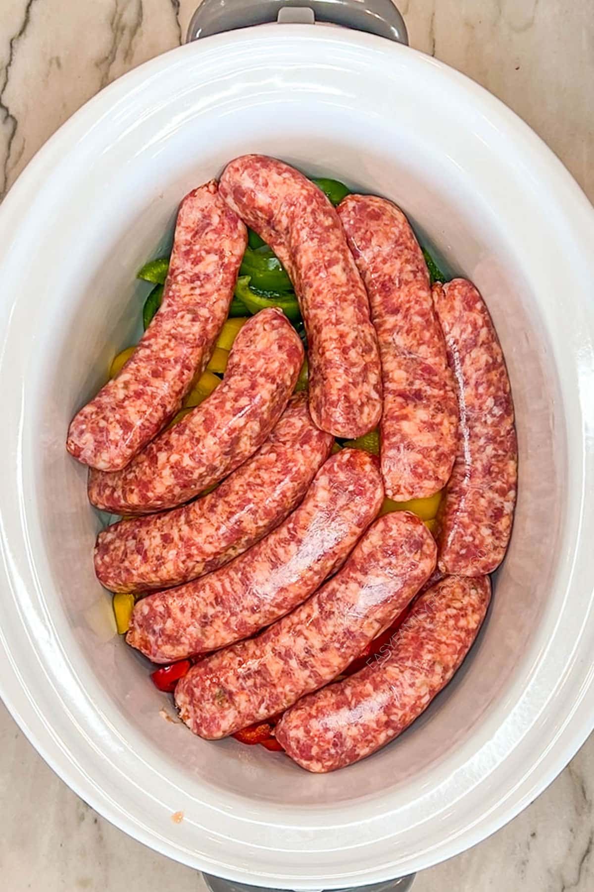 Peppers, onions and sausages added to a crockpot.