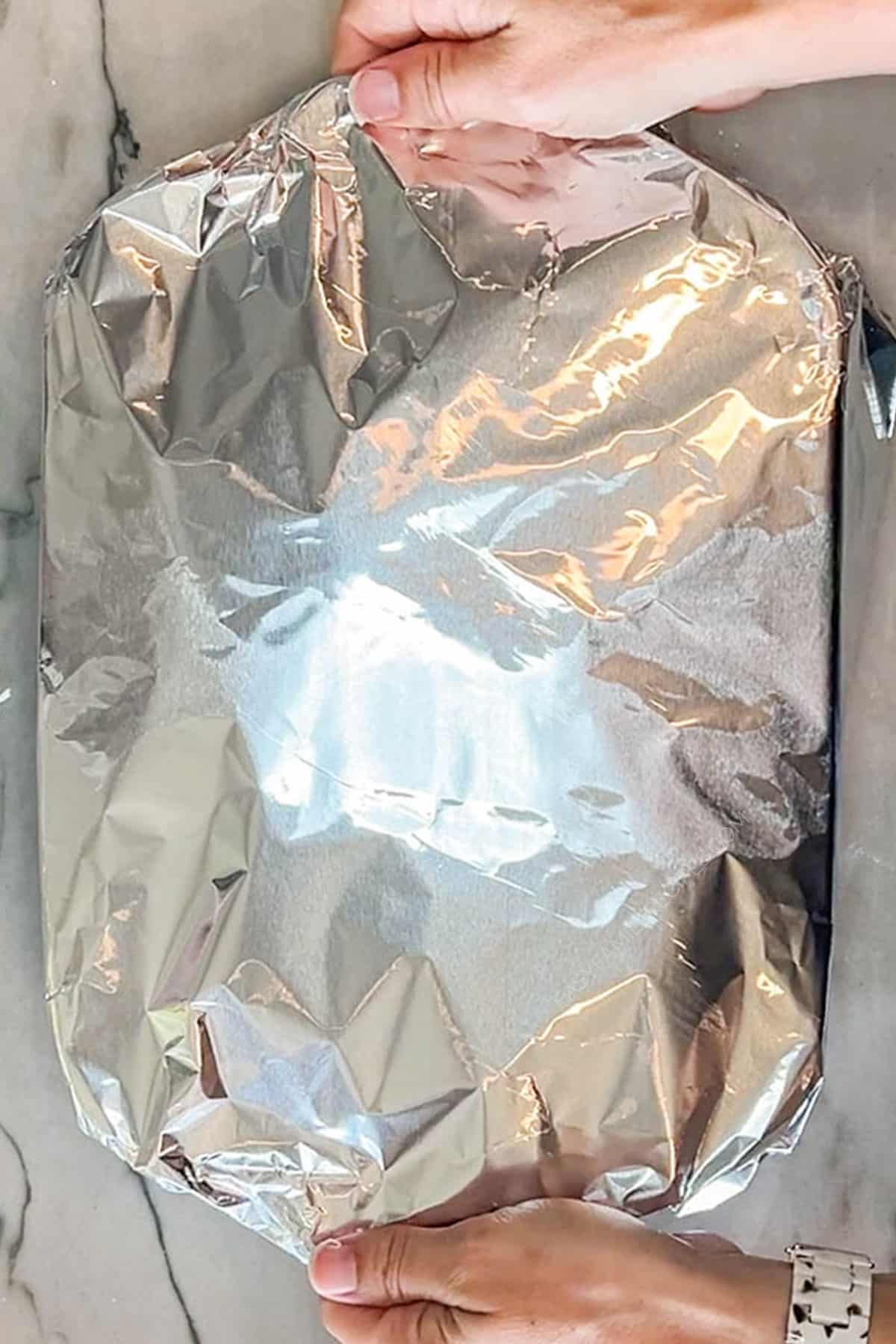 Hands placing foil on top of a baking dish.