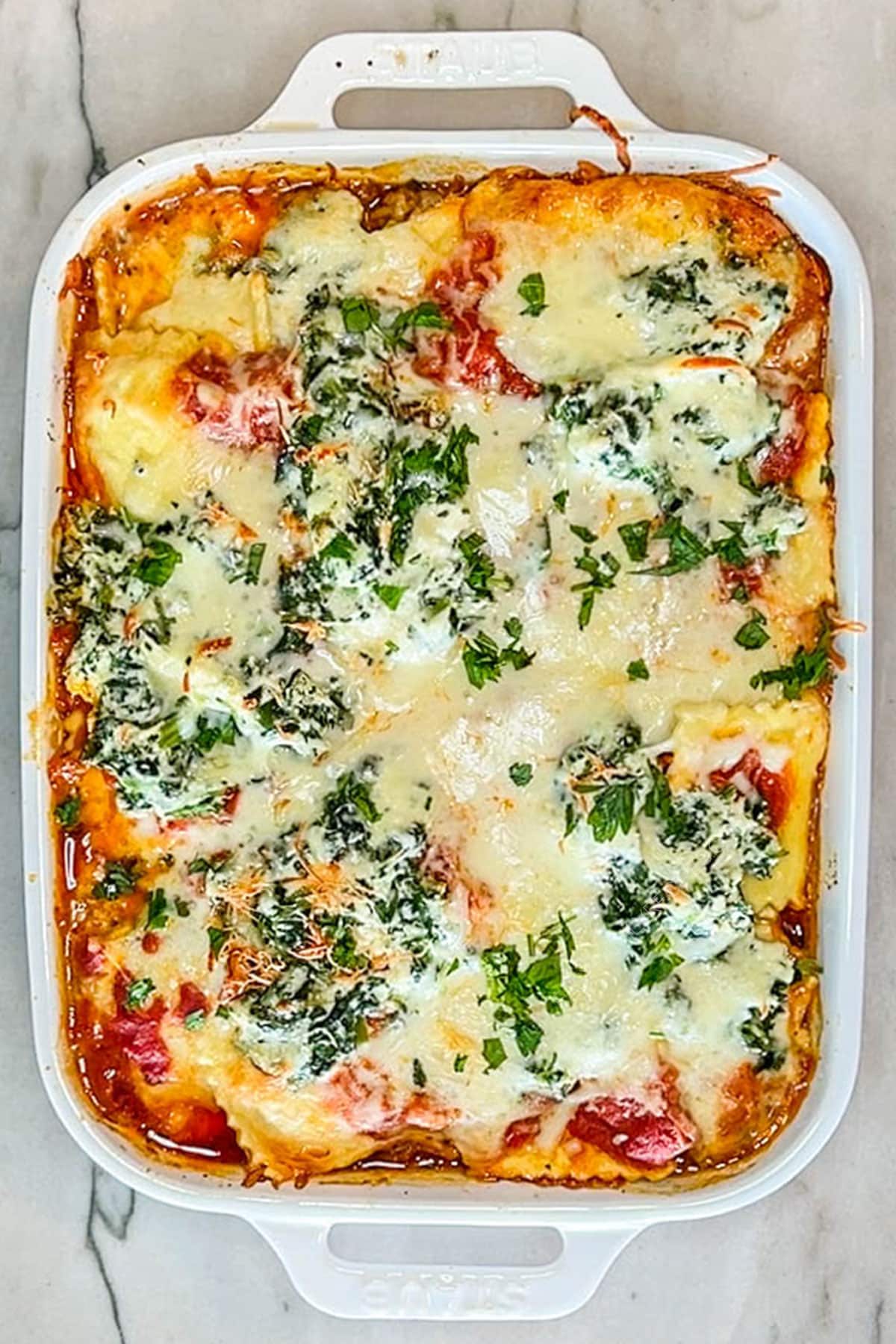 Overhead shot of baked ravioli lasagna in a white baking dish.