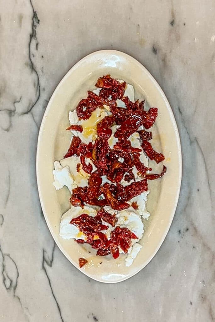 goat cheese on a plate layered with sun dried tomatoes.