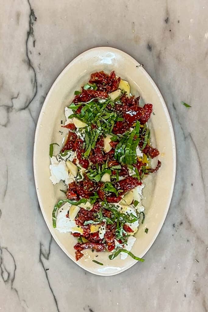 finished marinated goat cheese topped with herbs and sun dried tomatoes.