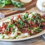 marinated goat cheese on a plate topped with sundried tomato and fresh herbs.