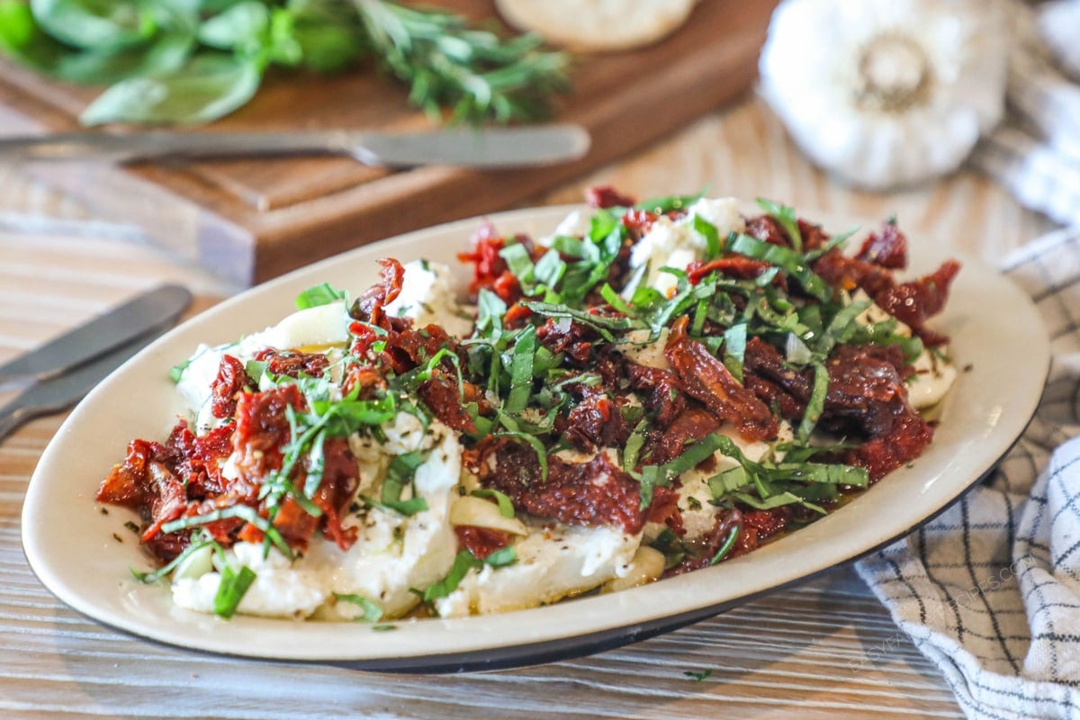 marinated goat cheese on a plate topped with sundried tomato and fresh herbs.