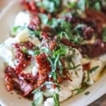 marinated goat cheese on a plate topped with sundried tomato and fresh herbs.