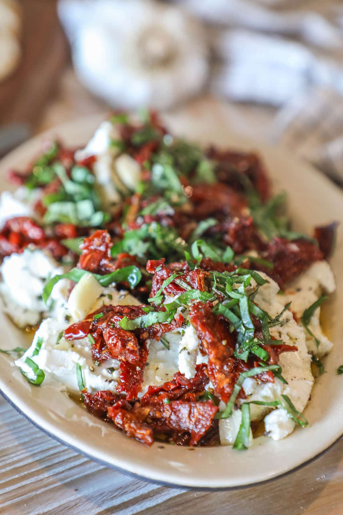 marinated goat cheese on a plate topped with sundried tomato and fresh herbs.