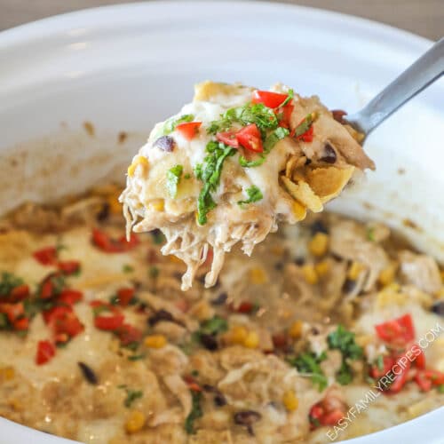 Spoon scooping up a portion of crockpot green chicken enchiladas from a slow cooker.