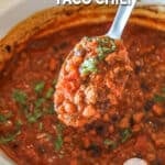 Spoonful of crockpot taco chili hovering over the crockpot of chili.