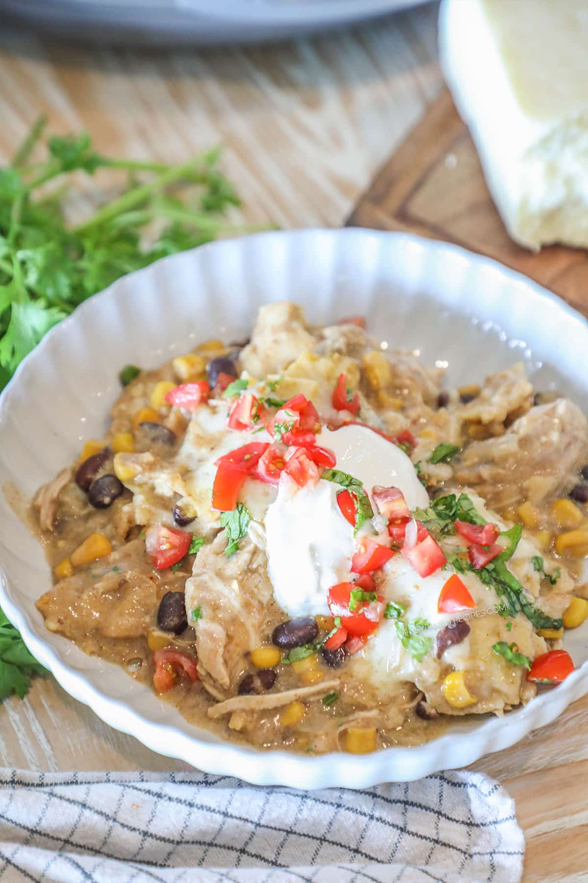 Crockpot green chicken enchiladas served in a bowl with sour cream with tomatoes on top.