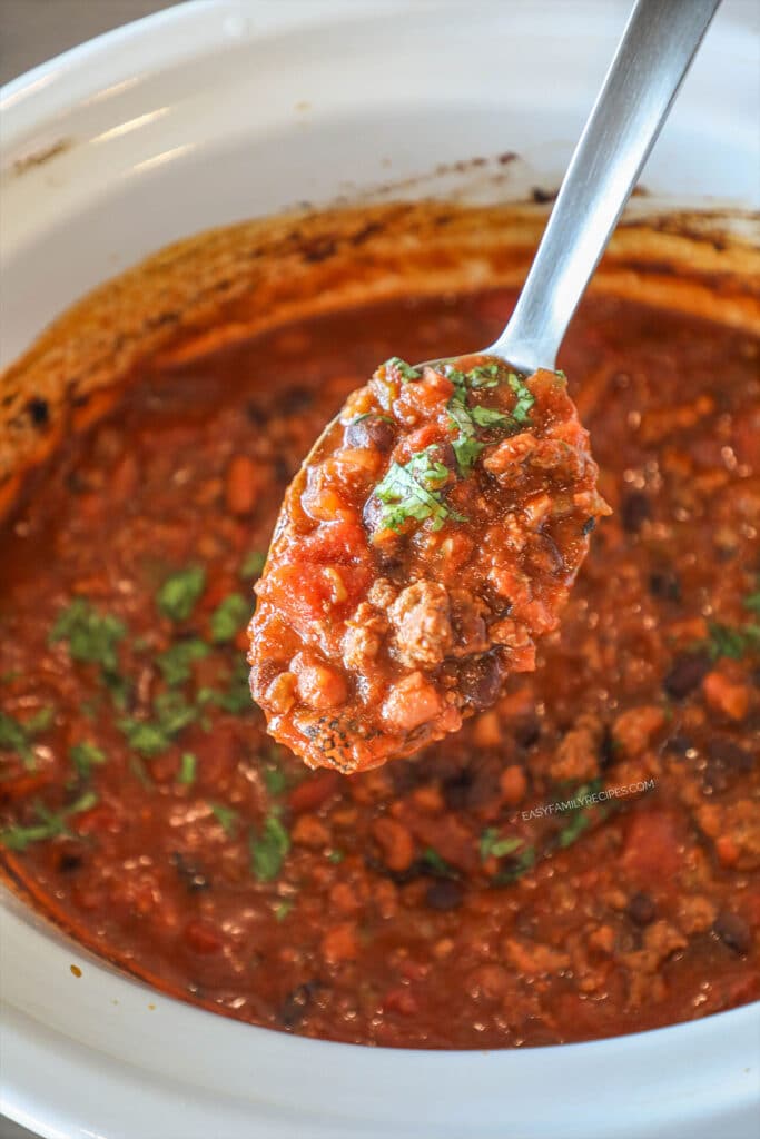 Serving spoon with chili on it, hovering over the slow cooker of taco chili.