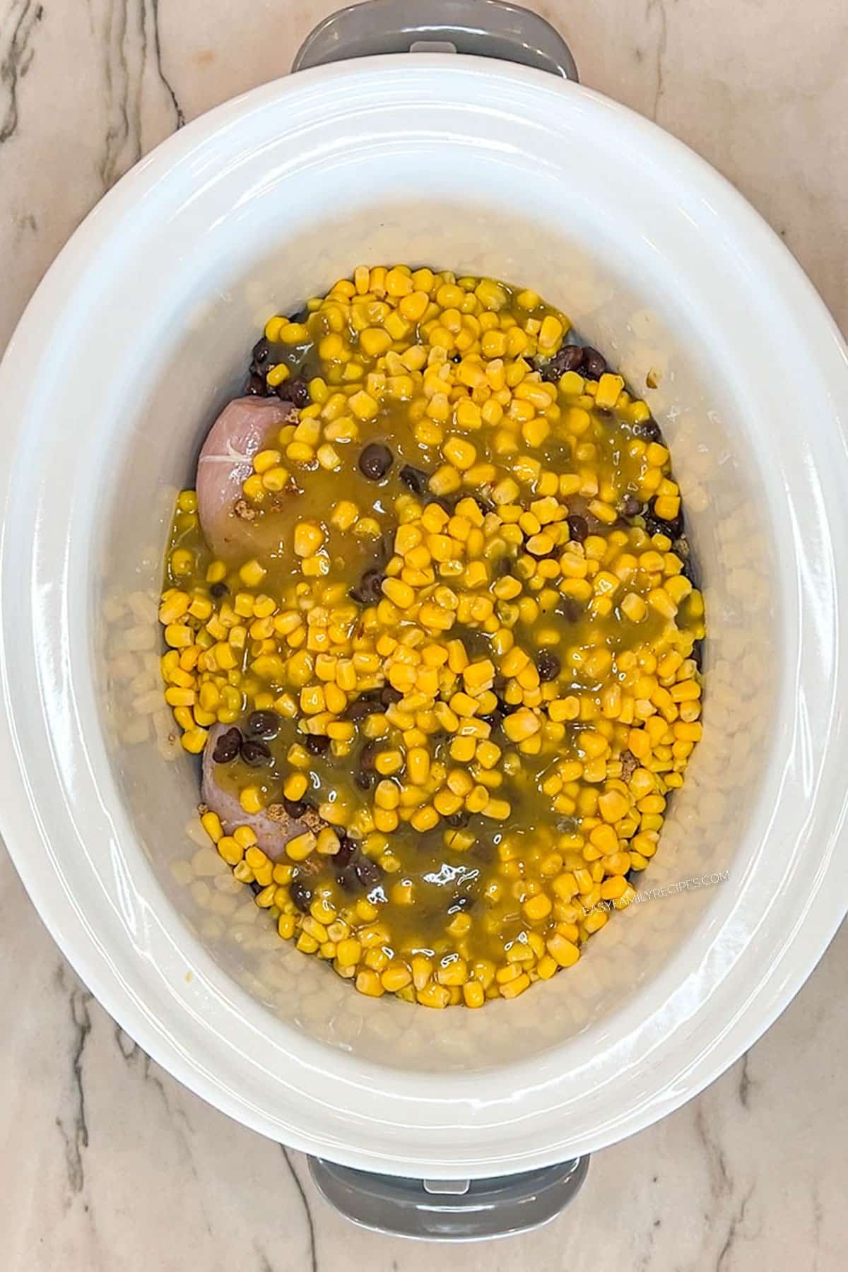 Chicken breast, corn, beans, and green salsa in a slow cooker.