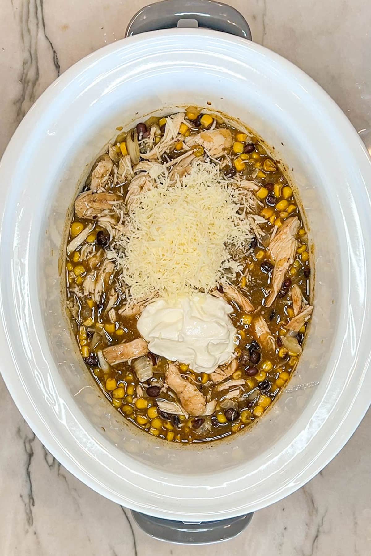 Cheese and sour cream added to the chicken enchiladas in a crockpot.