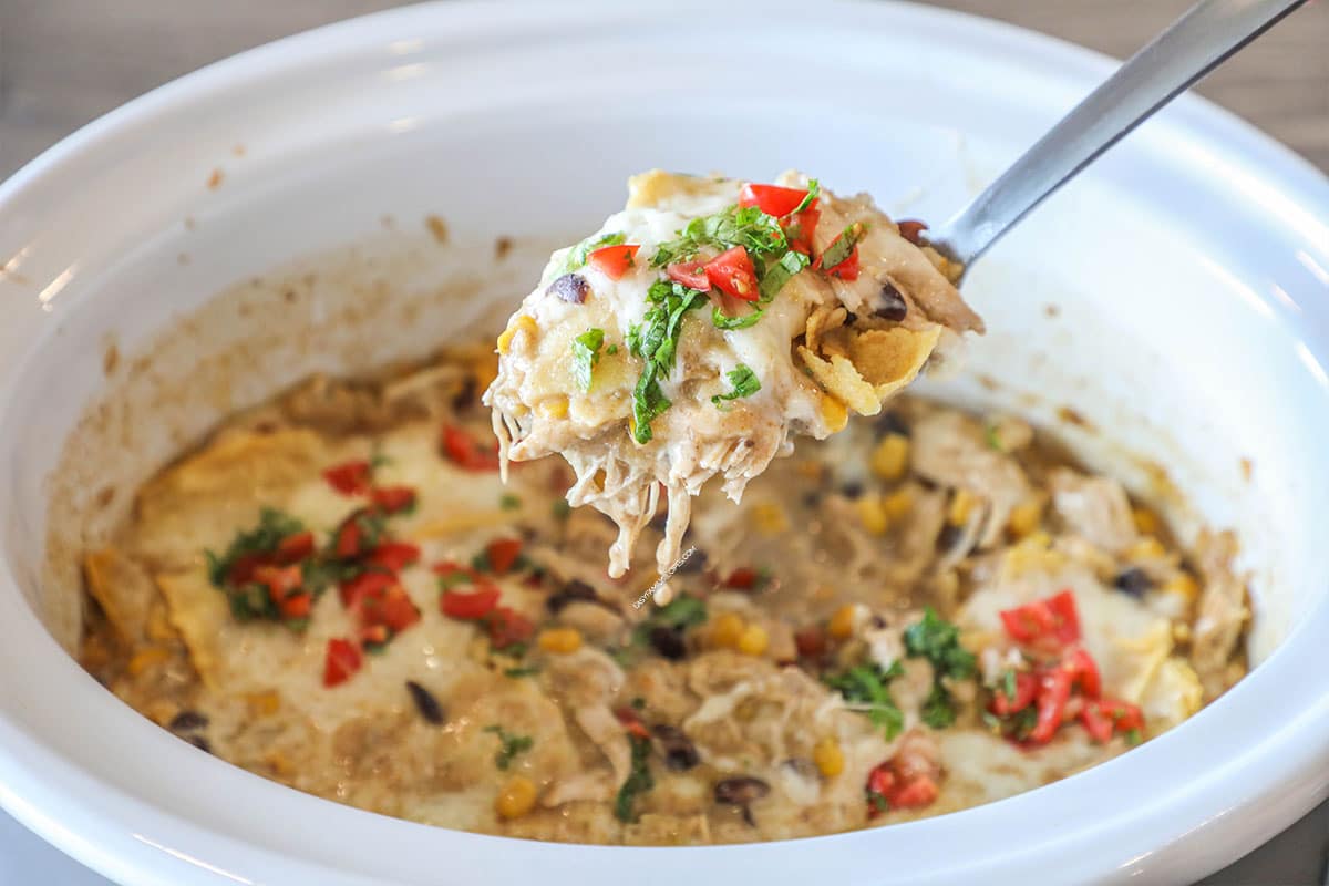 Crockpot of crockpot chicken enchiladas with a spoon scooping some up.