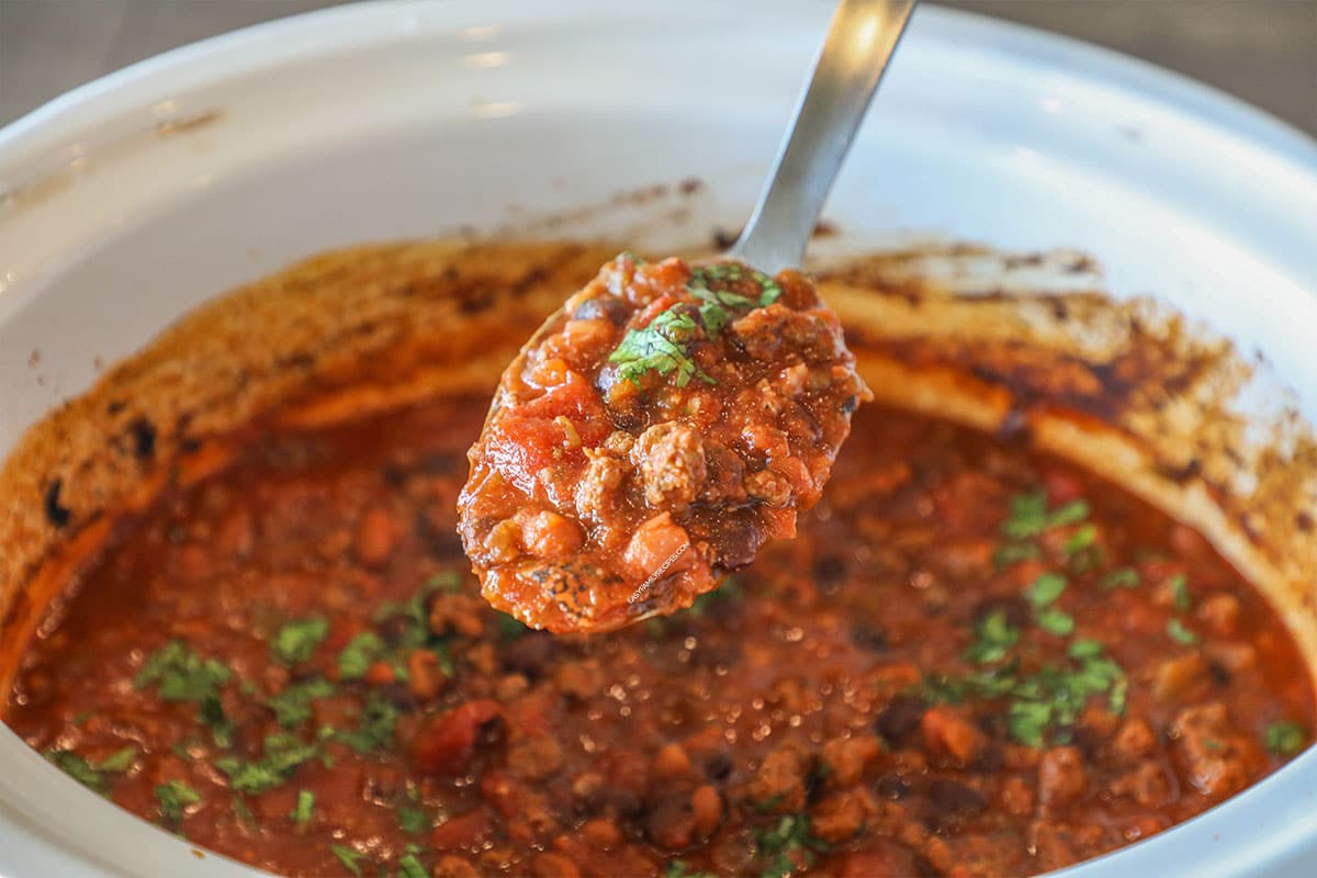 Serving spoon with a portion of taco chili on it, hovering over a crockpot.
