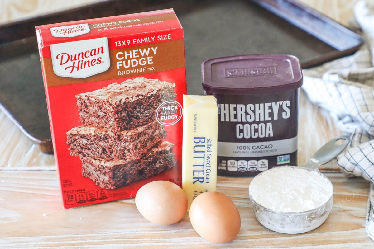Ingredients needed to make Brownie Crinkle Cookies- on a wooden background with a sheet pan and towel