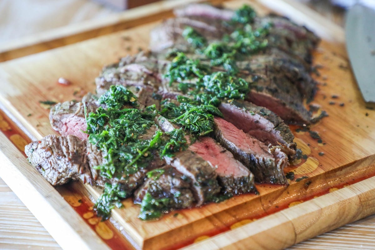Chimichurri Flank Steak grilled, sliced and topped with fresh chimichurri sauce. On a wooden cutting board