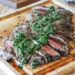 Chimichurri Flank Steak grilled, sliced and topped with fresh chimichurri sauce. On a wooden cutting board