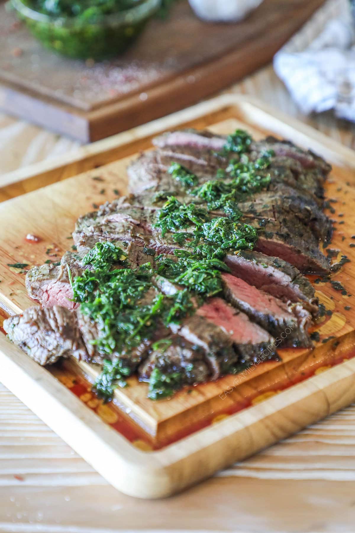 Chimichurri Flank Steak grilled, sliced and topped with fresh chimichurri sauce. On a wooden cutting board