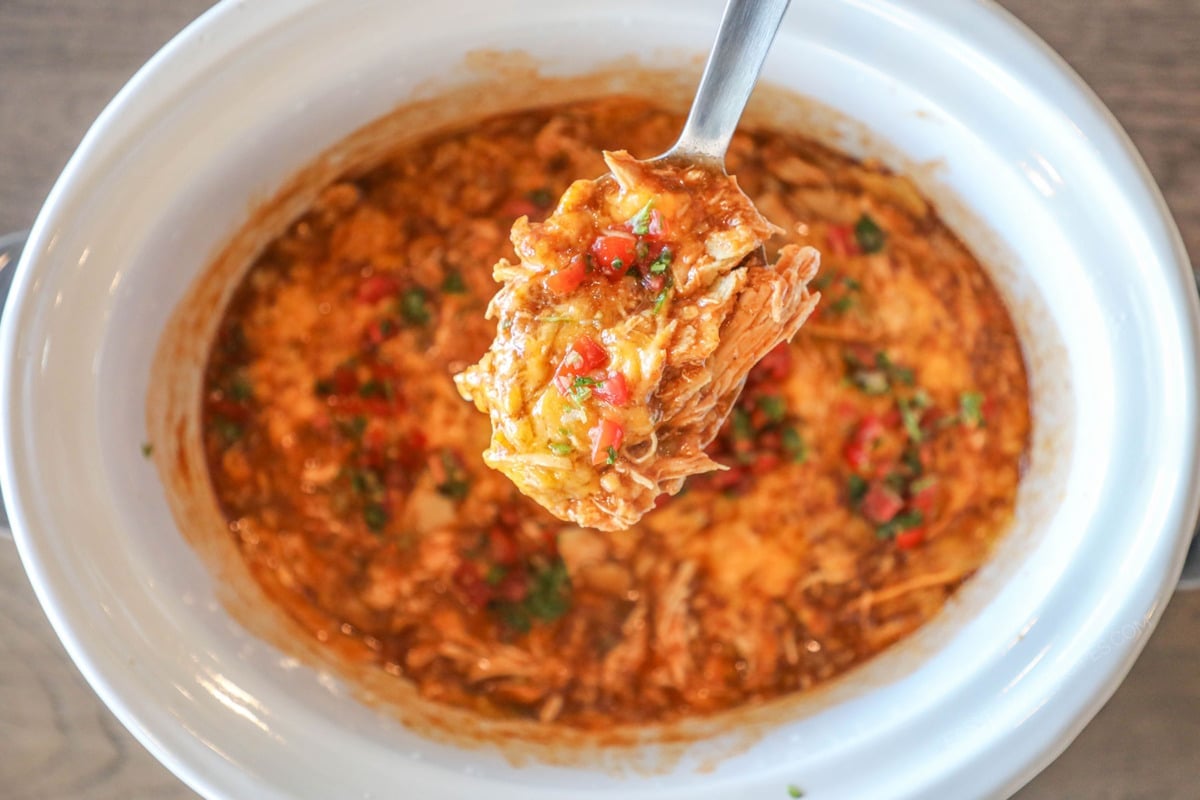 Crockpot Enchilada Chicken Casserole in white crockpot with spoon lifting out