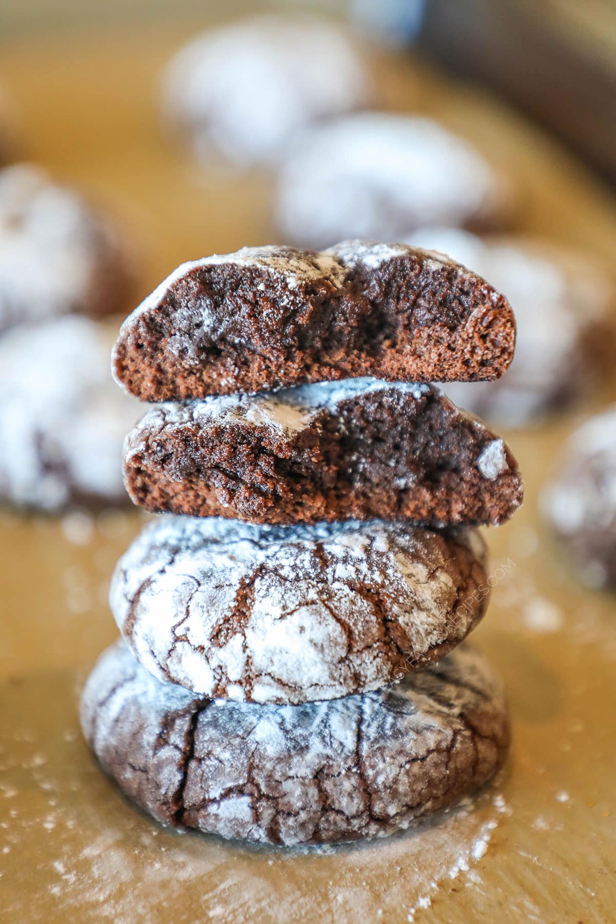 Brownie Crinkle Cookies stacked- top cookies show fudgy inside- on a parchment paper background