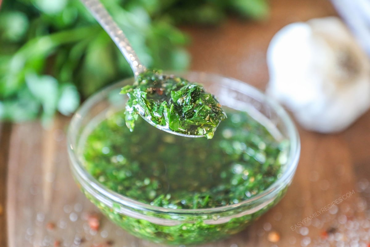 a scoop of homemade chimichurri being taken out of a bowl with a spoon.