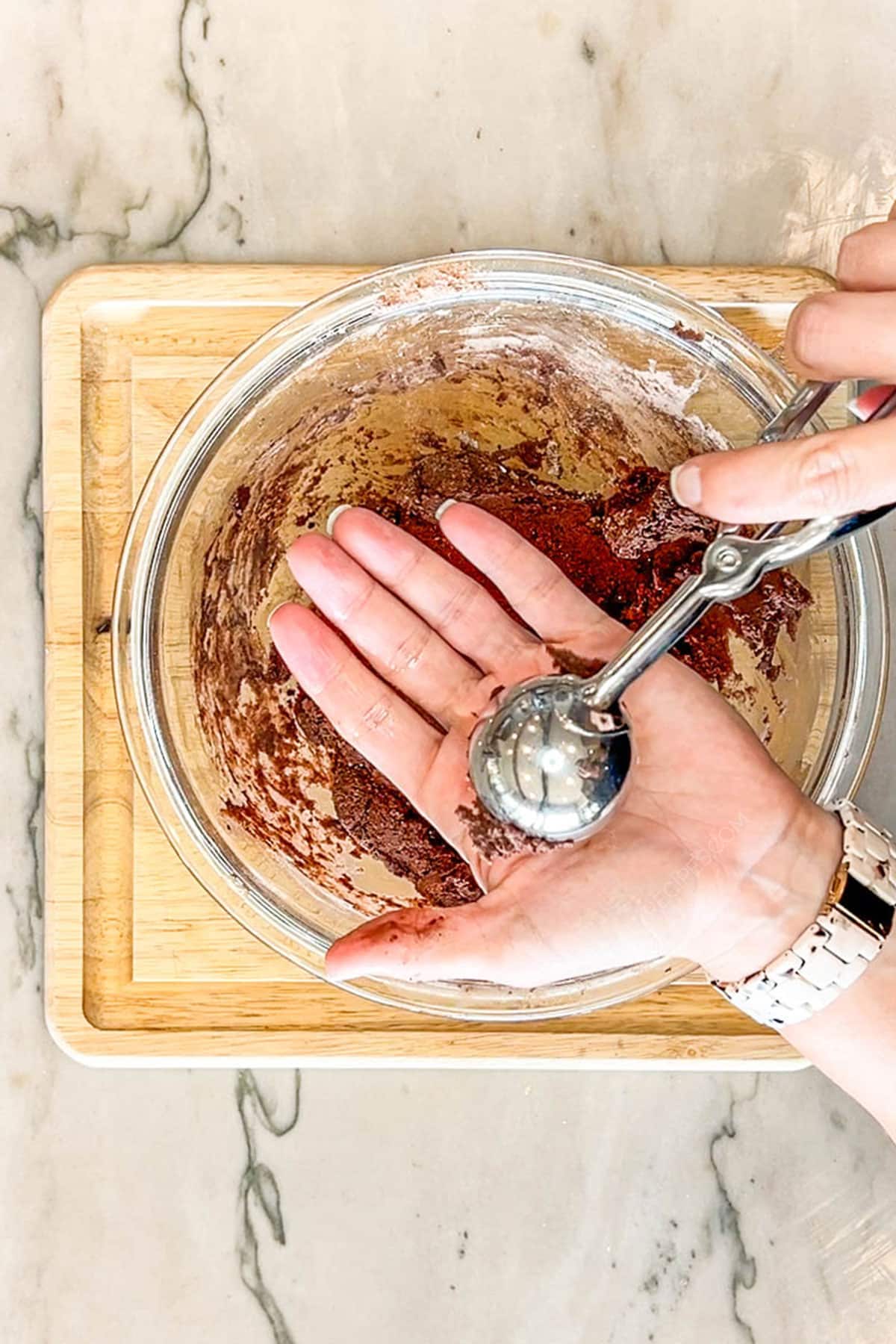 Step 2 for making Brownie Crinkle Cookies- mix ingredients together and scoop- image shows a scoop and hand