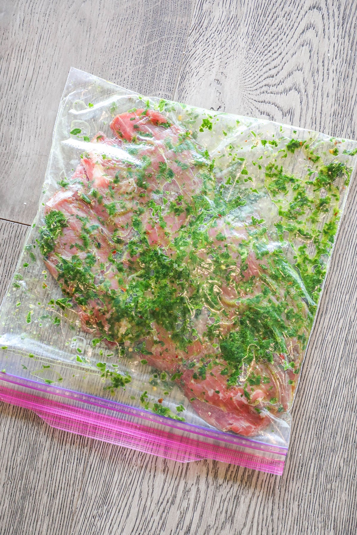 Flank steak marinating in chimichurri. In a ziptop plastic bag. On a wooden background