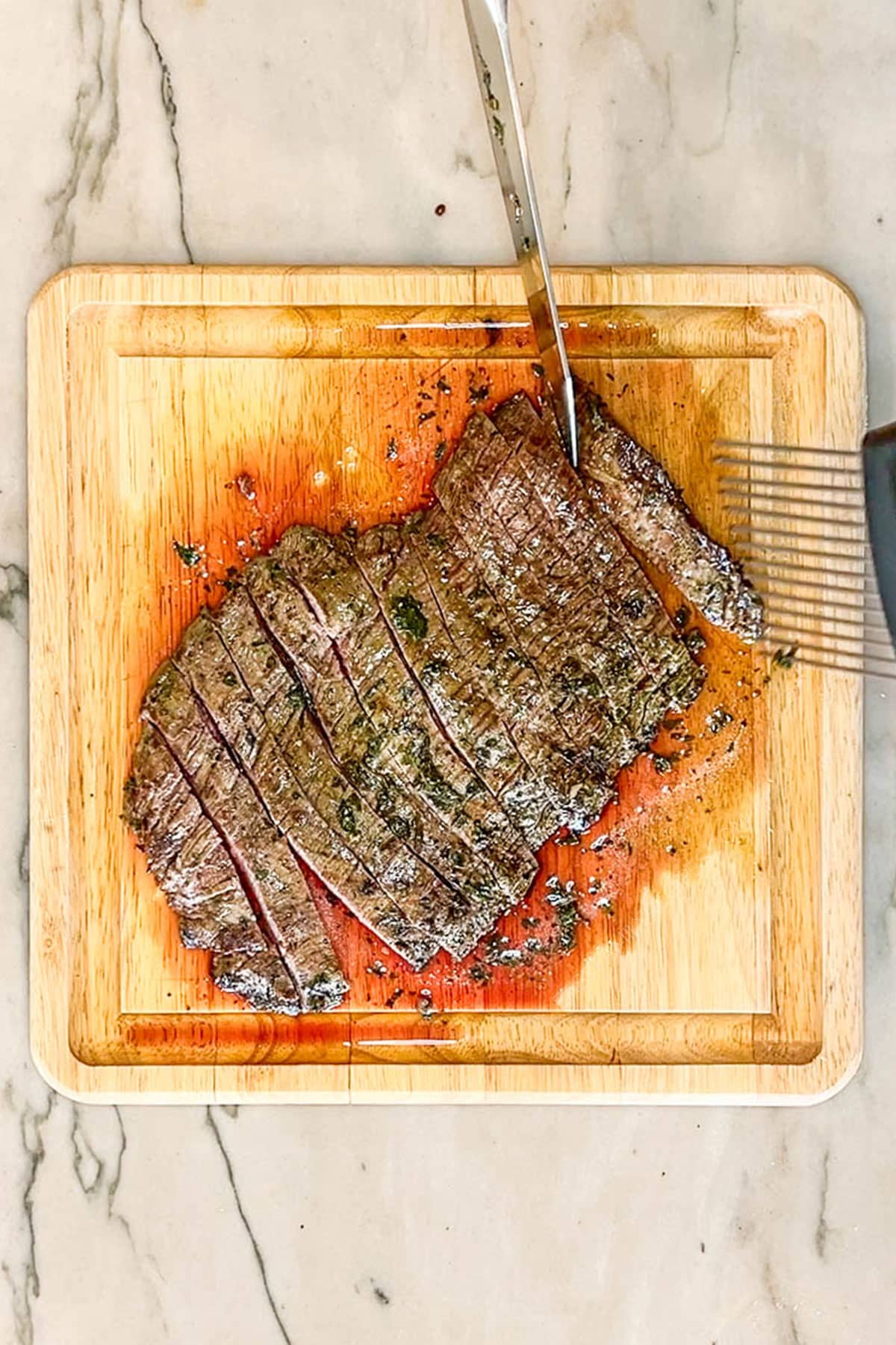 Grilled and sliced chimichurri flank steak on a wooden cutting board, with a knife