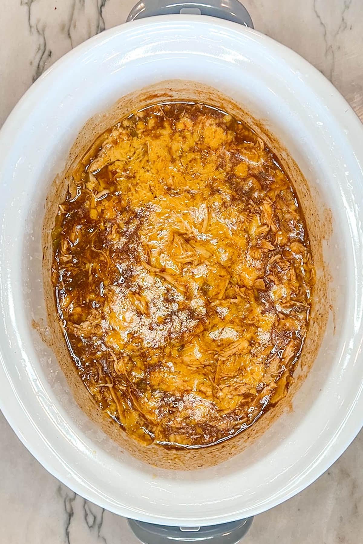 Crockpot Enchilada Chicken Casserole step 3. Cheese added to cooked chicken. In a white crockpot