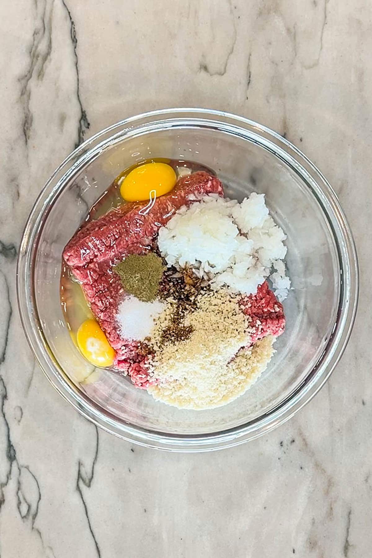 Step 1 for making Crockpot Meatloaf and Potatoes- meatloaf ingredients combined in glass bowl- on a marble background