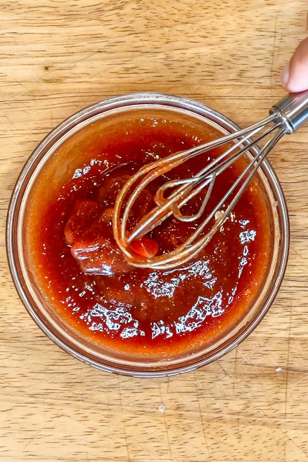 Step 3 for making Crockpot Meatloaf and Potatoes- ingredients for ketchup glaze in glass bowl with whisk- on a wooden background