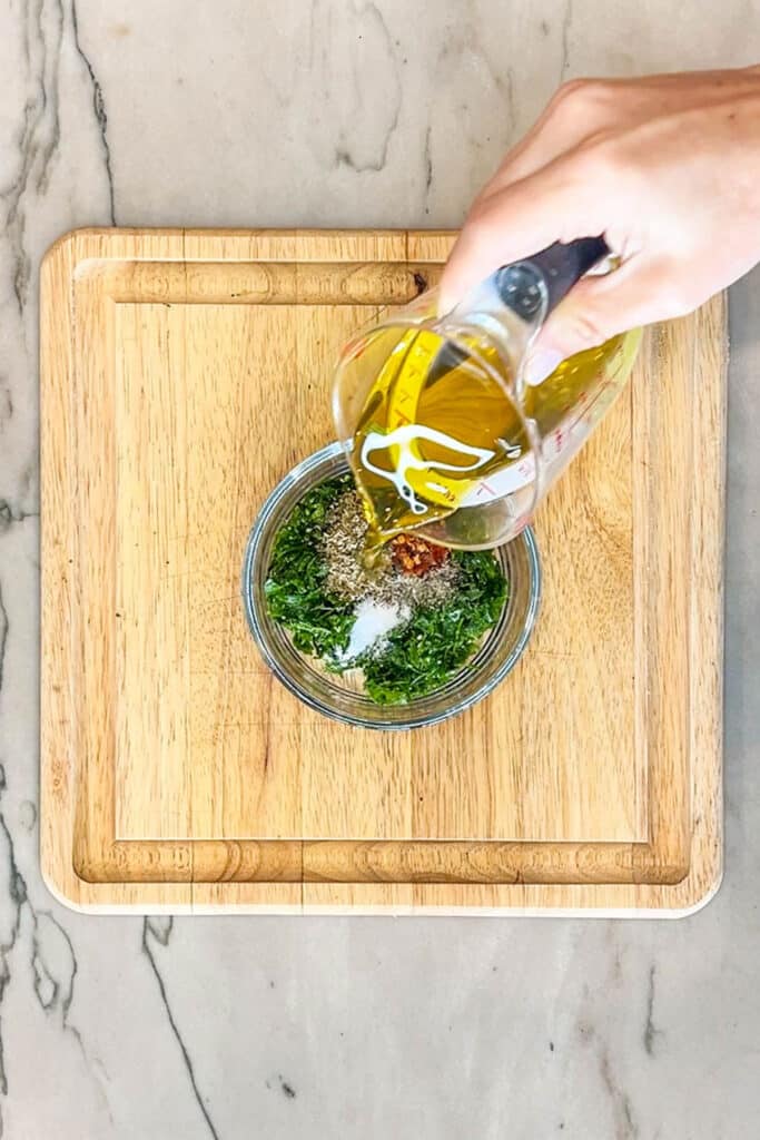oil being poured into a bowl with fresh parsley and garlic.