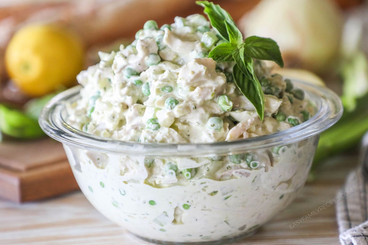 Glass bowl with pesto chicken salad and fresh basil leaves on top. On a wooden background with lemon.