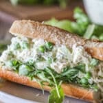 Baguette stuffed with arugula and pesto chicken salad. Wooden board in background