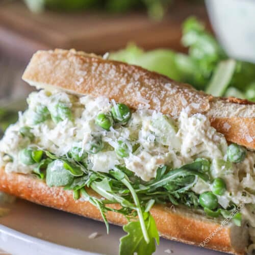 Baguette stuffed with arugula and pesto chicken salad. Wooden board in background