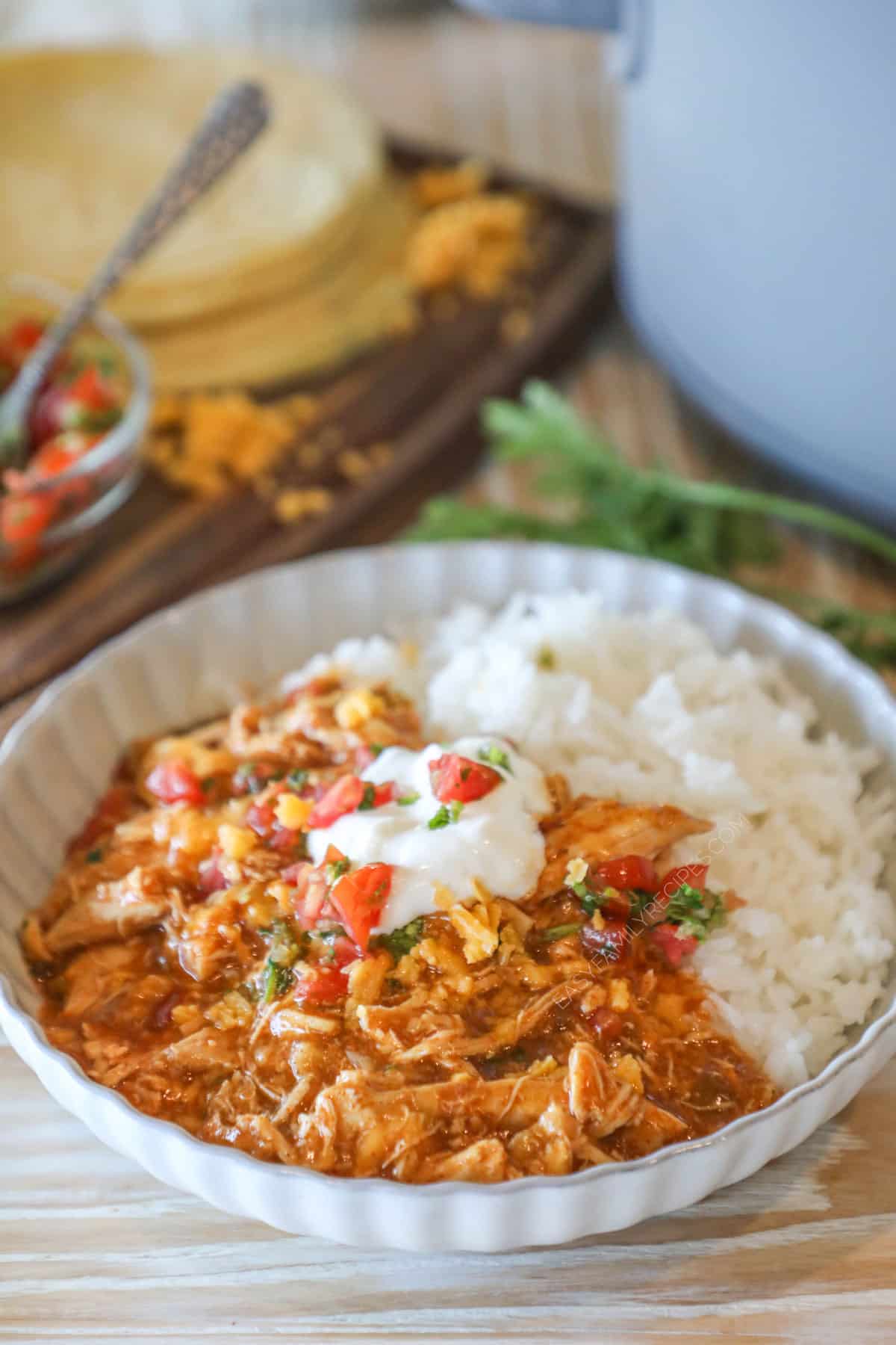 Crockpot Enchilada Chicken Casserole with a side of rice on a white dish. Tortillas and pico de gallo in background