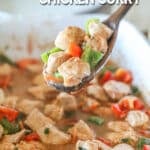 Wooden spoon scooping up baked chicken curry from a baking dish.