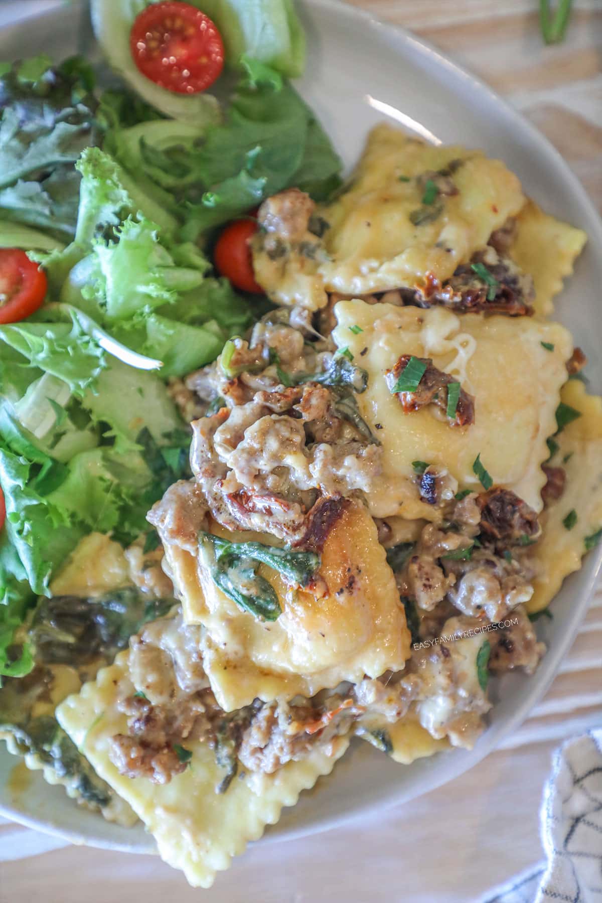 Marry Me Ravioli Casserole individual serving on white plate with side salad. On a wooden background