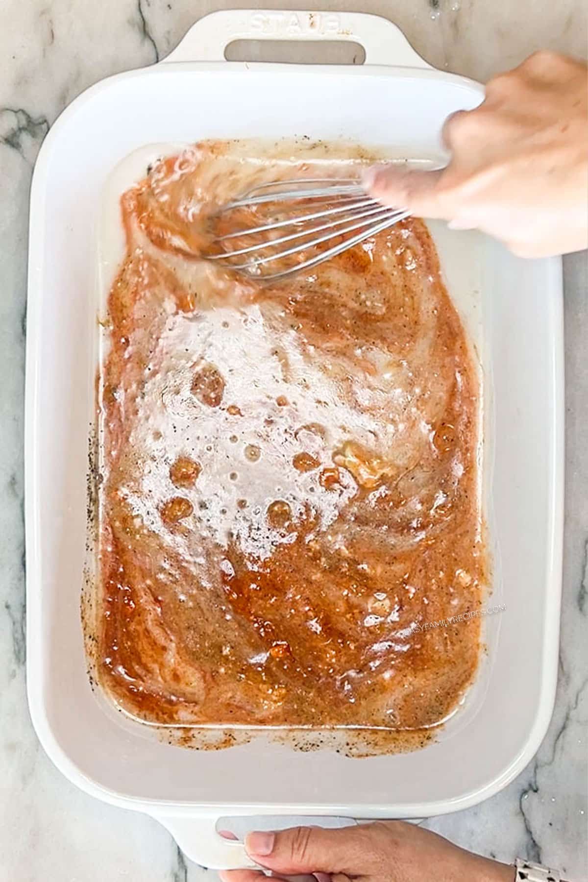 Hands whisking together the coconut milk curry sauce in the bottom of a baking dish.