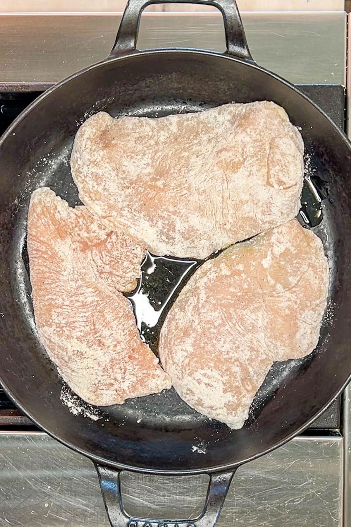 Searing dredged chicken breast in a skillet.