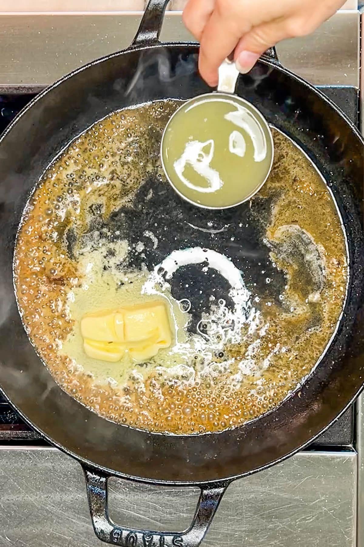 Adding chicken broth to the lemon butter sauce in a skillet.