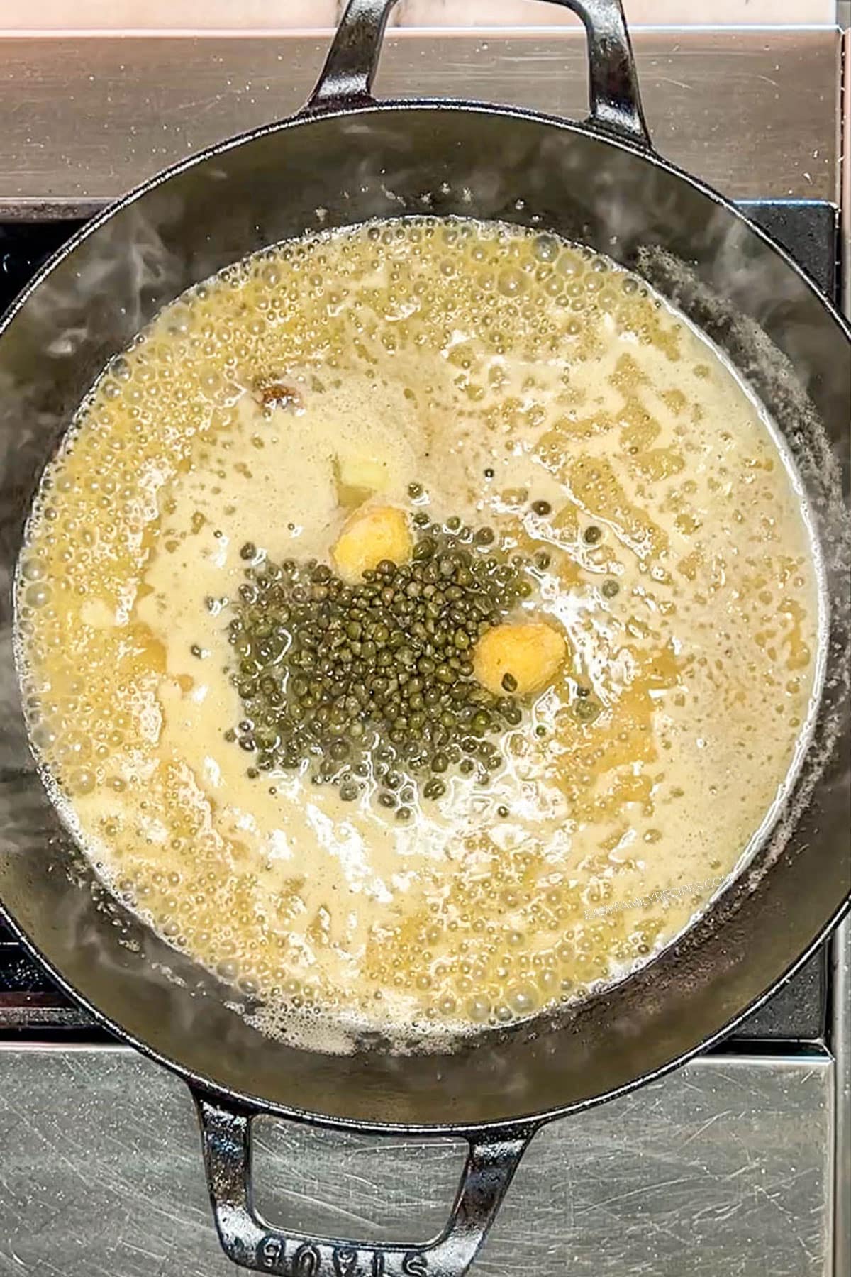 Adding capers and garlic to the chicken piccata sauce.