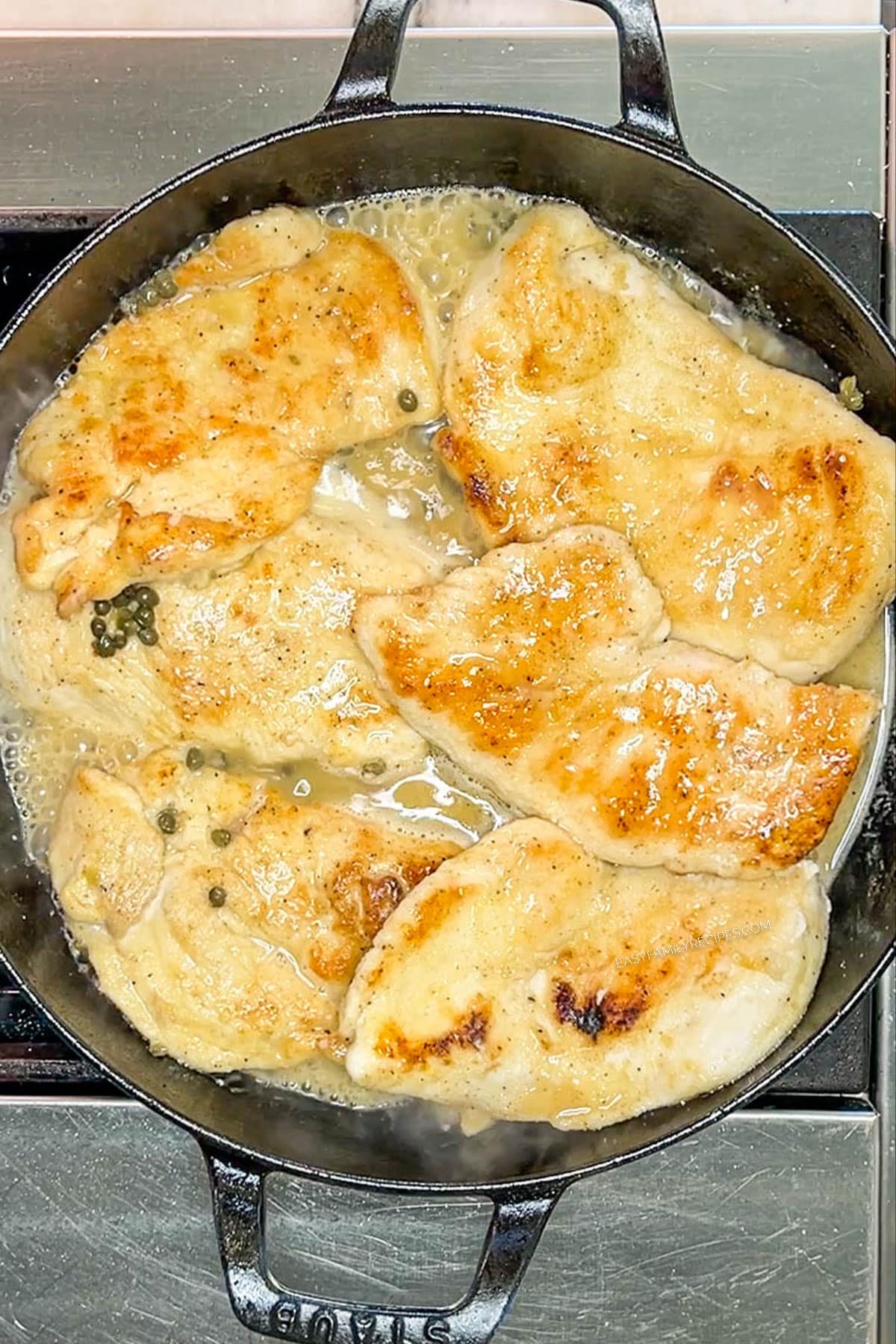 Chicken added back into the lemon sauce in a skillet.
