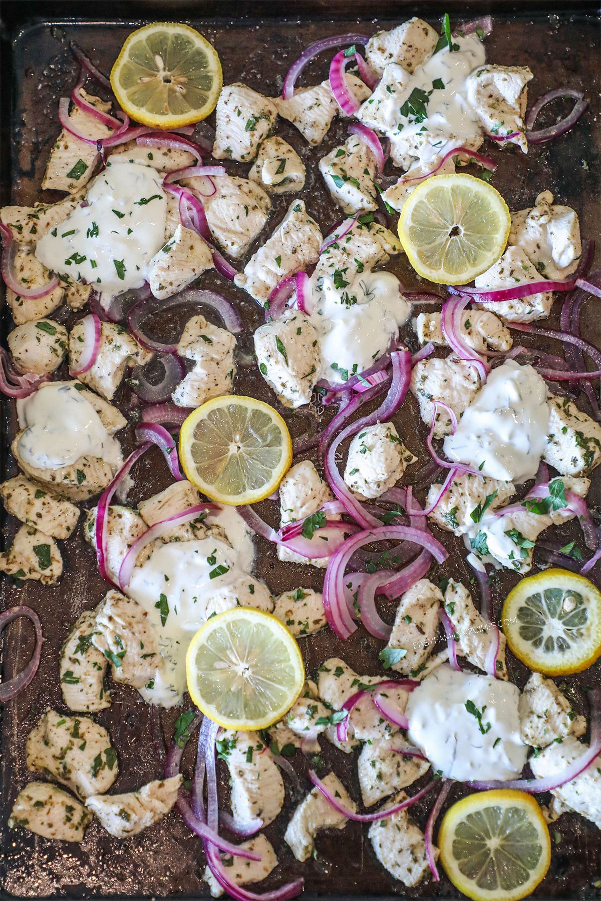 Sheet pan of cooked greek chicken, sliced red onion and lemon slices