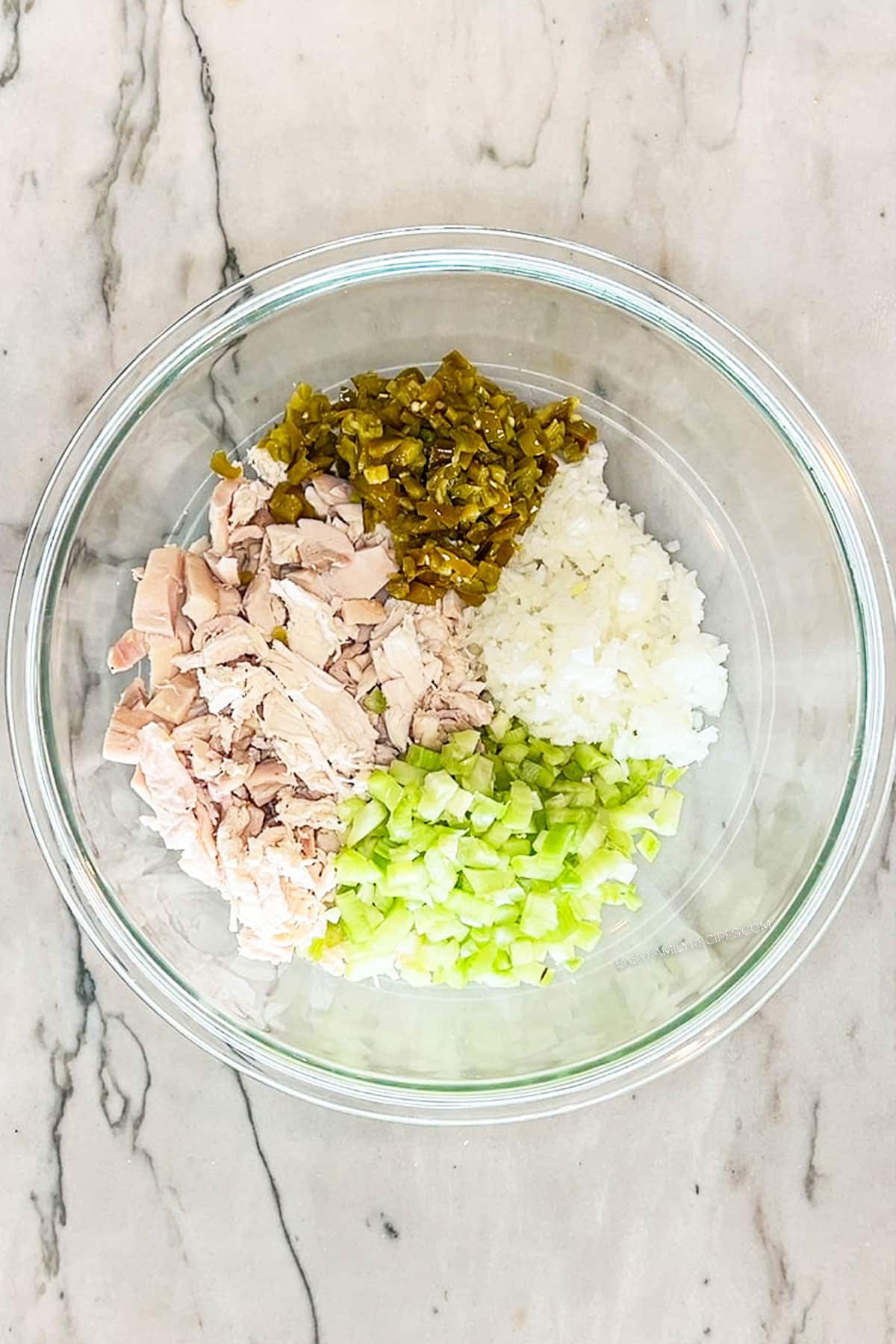 Step 1 for making Jalapeño Popper Chicken Salad. Chicken, jalapeños, onion and celery in a glass bowl