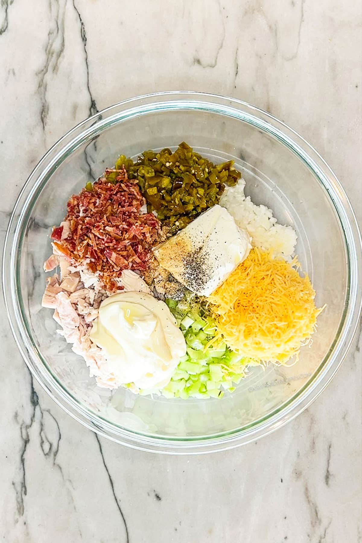 Step 2 for making Jalapeño Popper Chicken Salad. All ingredients in glass bowl, on a marble background