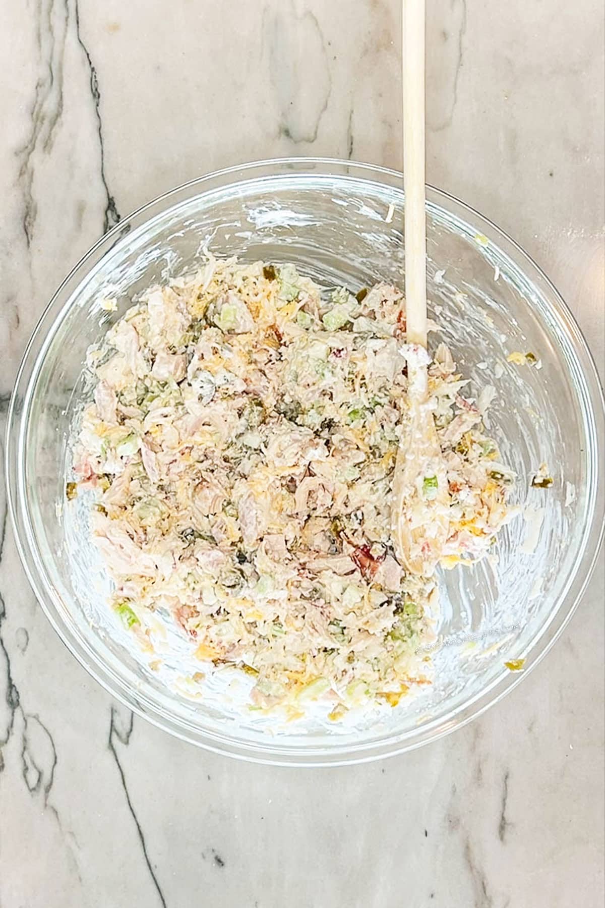 Step 3 for making Jalapeño Popper Chicken Salad. mix all ingredients together. In a glass bowl on a marble background.
