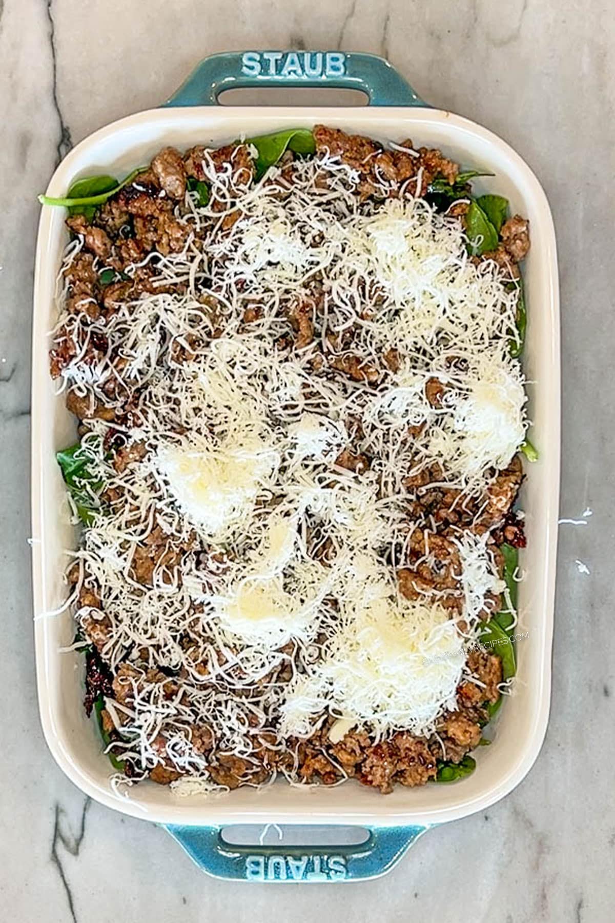 Step 3 for making Marry Me Baked Ravioli Casserole. Add Italian sausage and mozzarella cheese. In a blue baking dish on a marble background