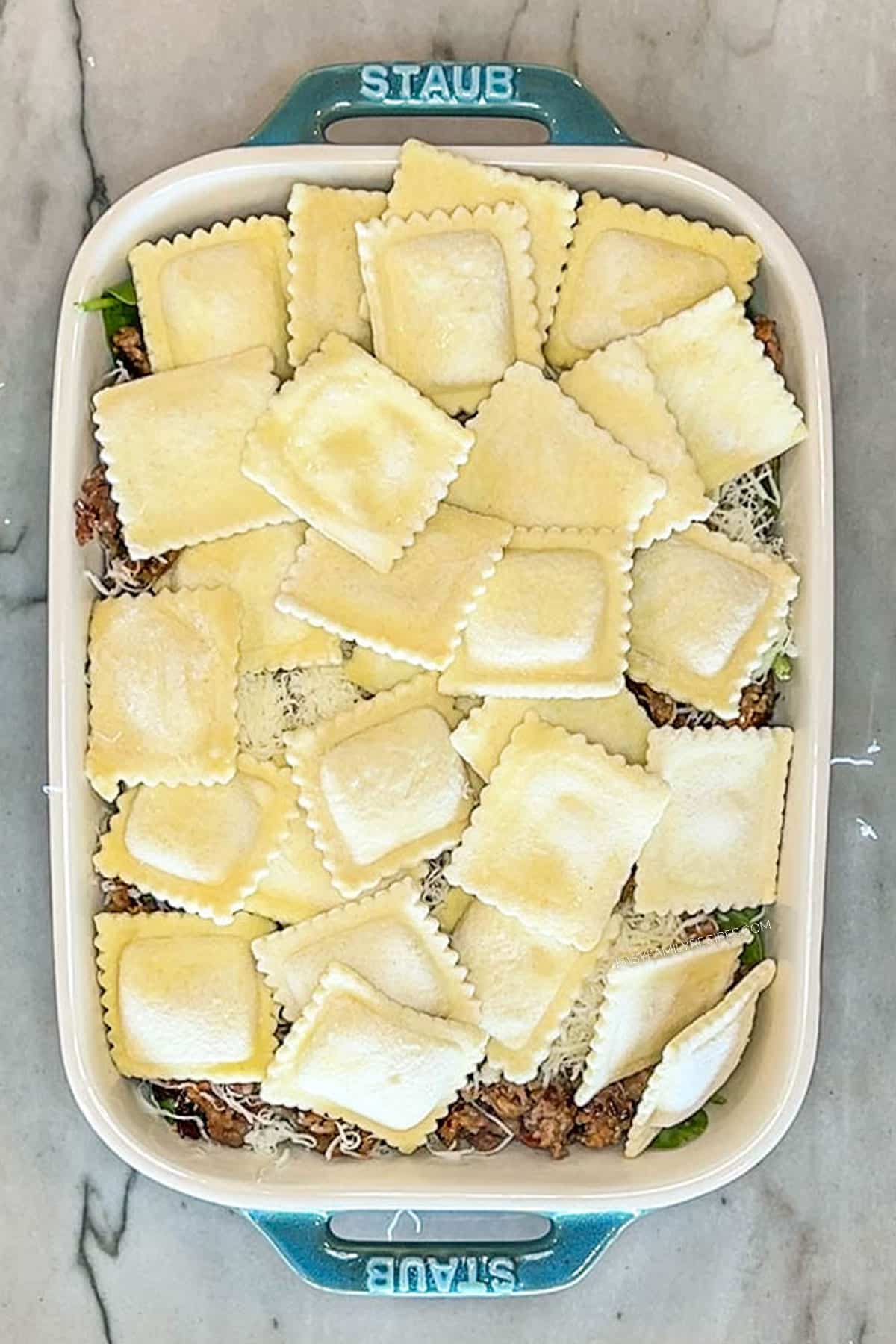 Step 4 for making Marry Me Baked Ravioli Casserole. Add another layer of ravioli. In a blue casserole dish on a marble background