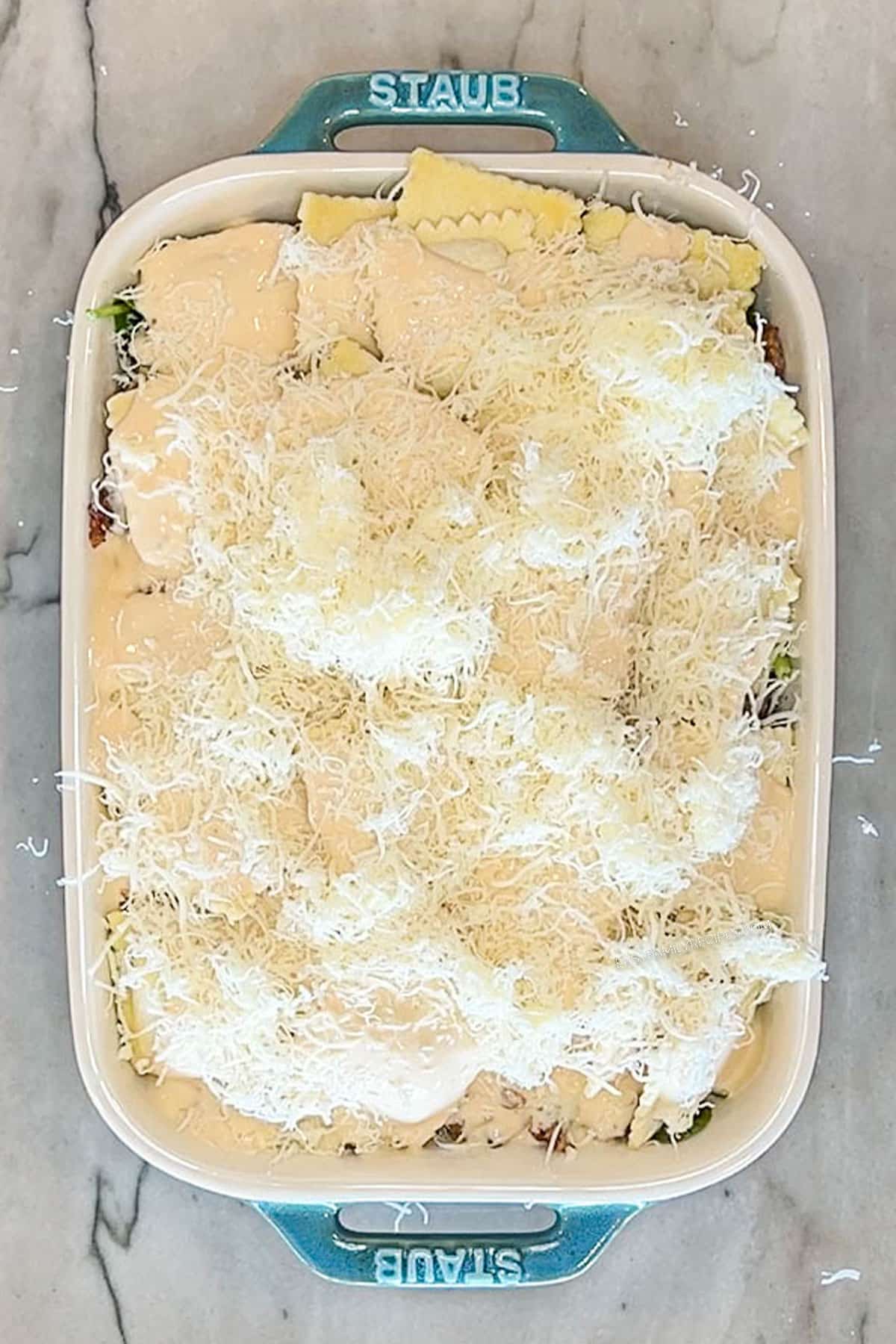 Step 5 for making Marry Me Baked Ravioli Casserole. Add mozzarella cheese. In a blue casserole dish on a marble background